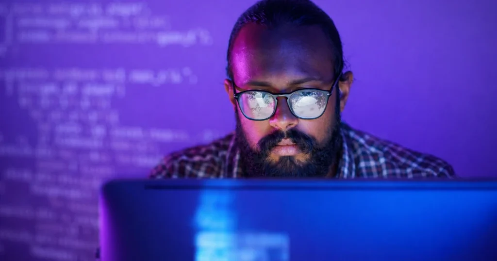 Cybersecurity professional focused on a computer screen, with glowing code and data displayed in a dark purple and blue environment.