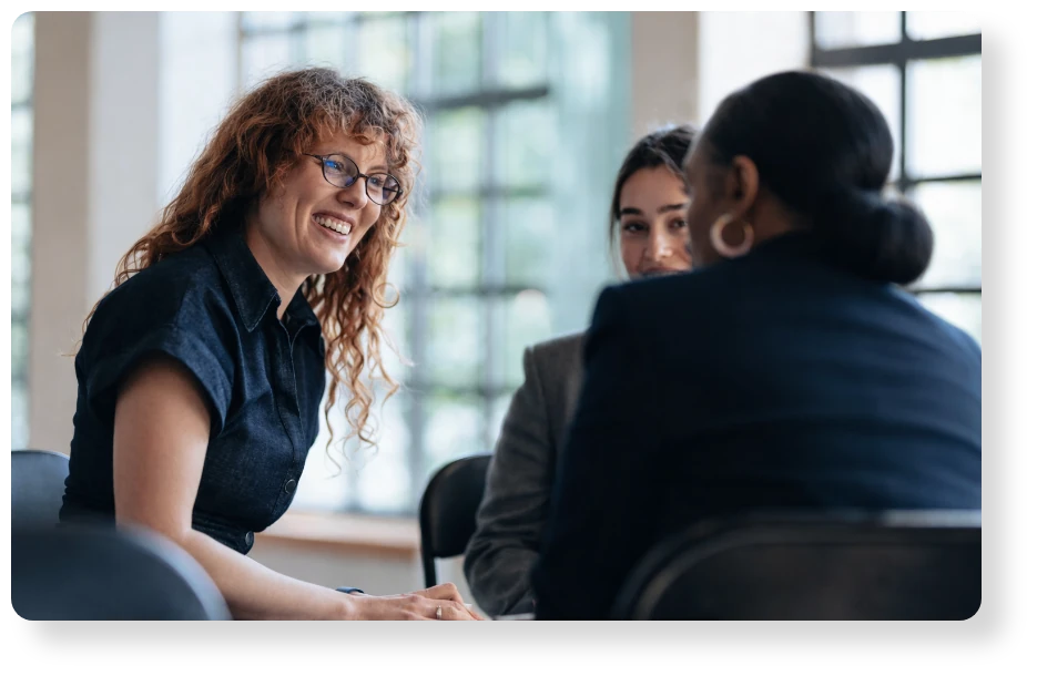 Three business professionals engaged in a friendly conversation during a meeting in a bright, modern office.