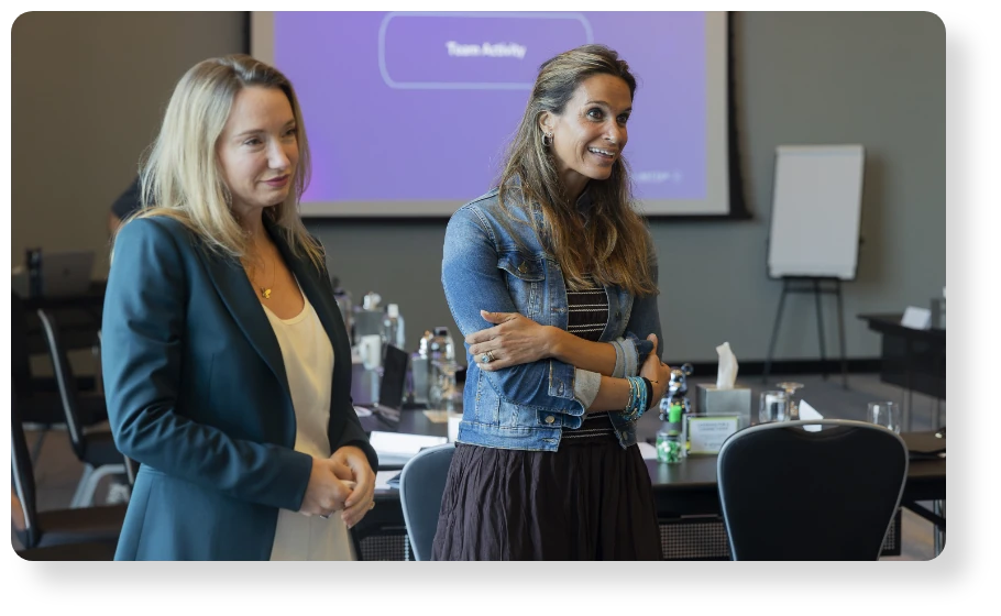 Two business professionals standing together during a workshop or team meeting in a modern conference room.